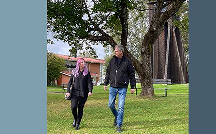 Två av våra upphandlare, Sara och Hans, promenerar vid klocktornet i Charlottenberg, blå bakgrund