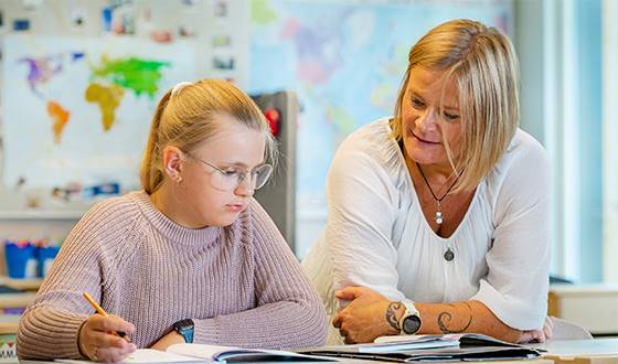 Kvinnlig lärare hjälper flicka vid skolbänk